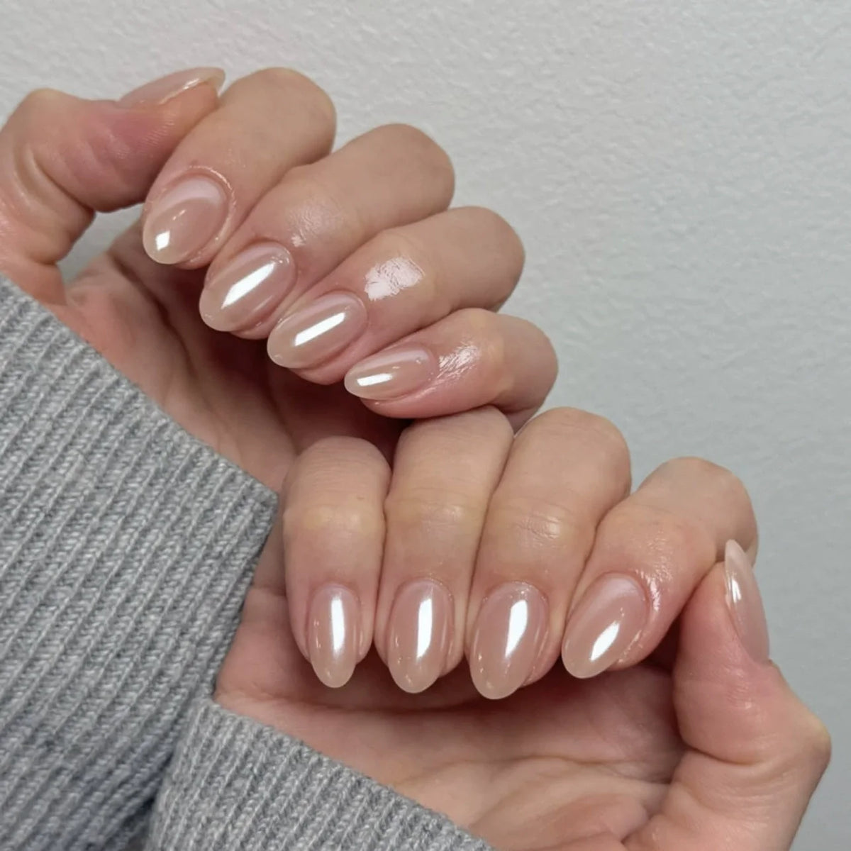 Two hands wearing short almond nude press-on nails with a glazed pearl finish